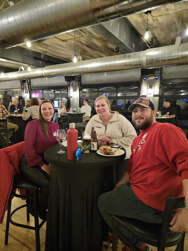 Three attendees sharing food and drinks at a high-top table
