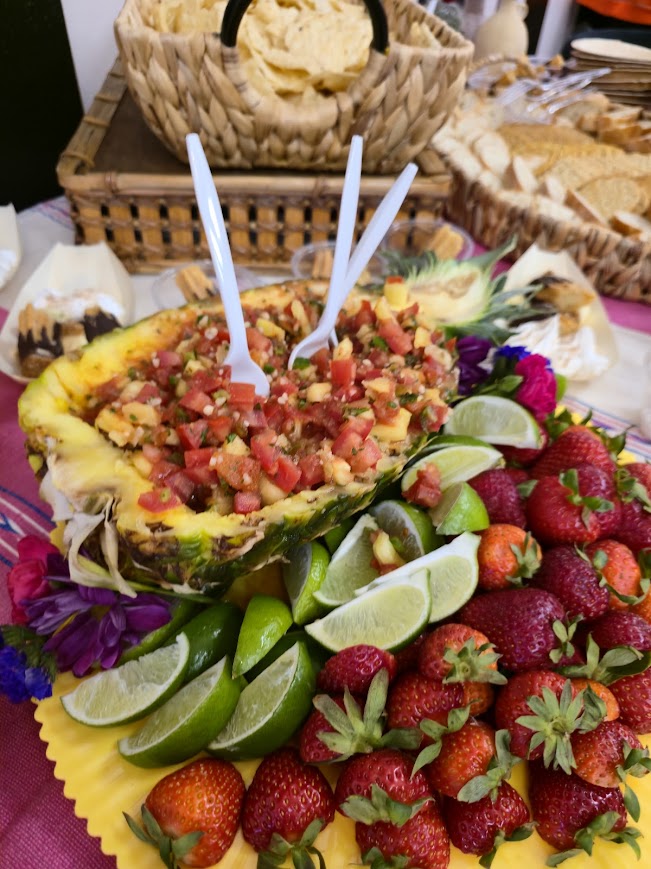 A pineapple salsa bowl surrounded by strawberries and lime wedges
