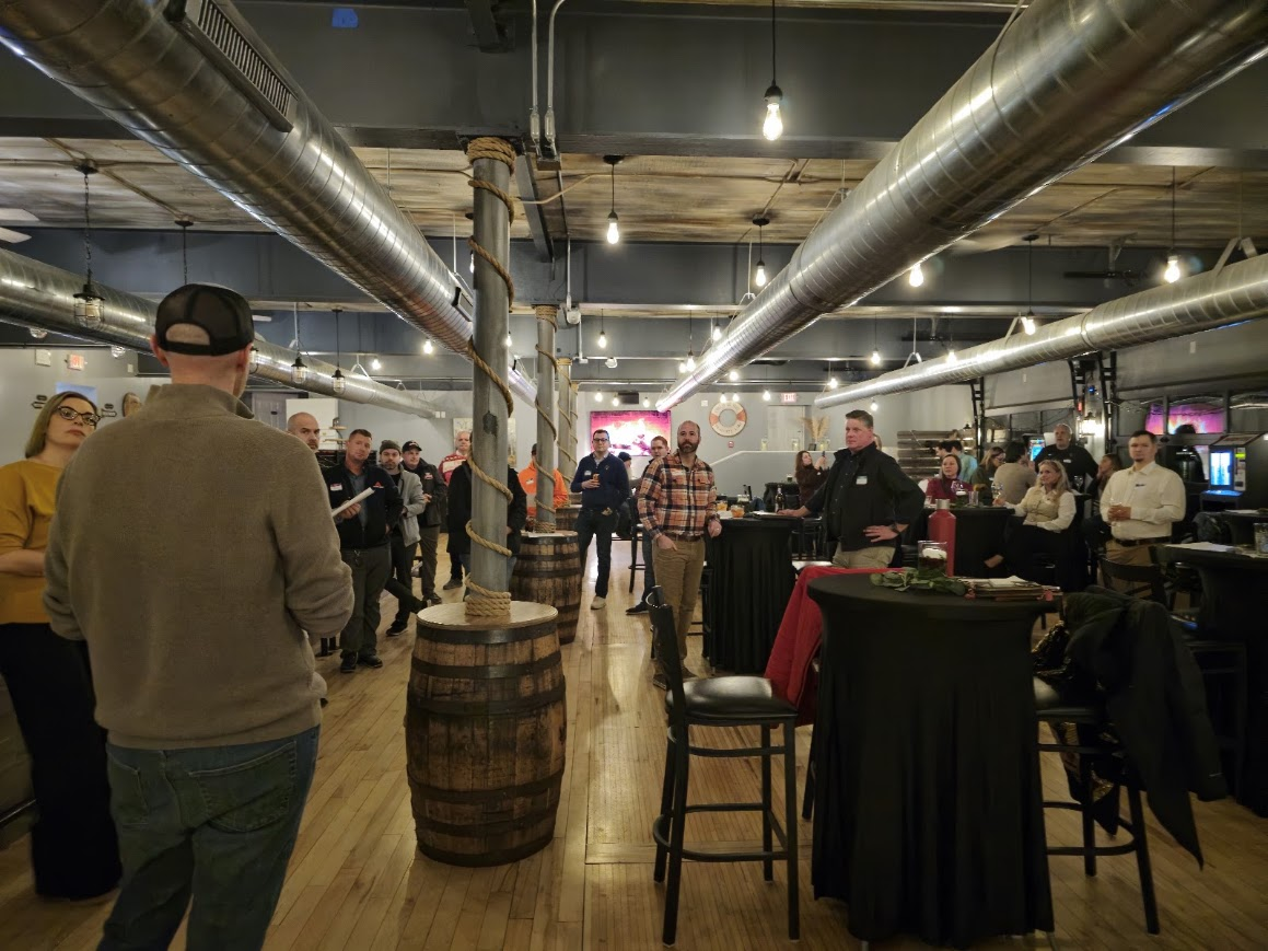 A host addressing a room of attendees standing among high-top tables at Smoke on the Water
