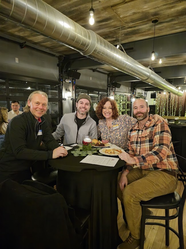Four attendees smiling around a high-top table at Smoke on the Water